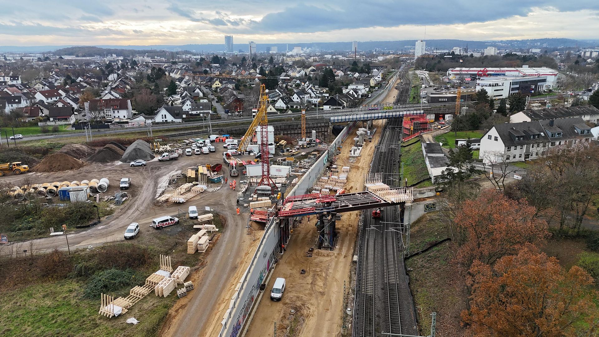 Vogelperspektive auf eine Bahnbaustelle. Zwei Brücken und Gleise sind zu sehen. Am Horizont ist die Bonner Skyline zu erkennen.