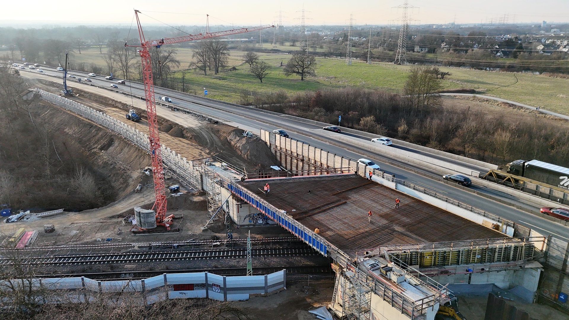 Blick auf eine Brückenbaustelle neben einer Autobahn. Daneben steht ein großer roter Kran.