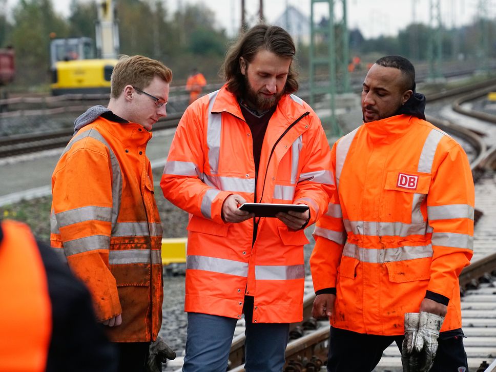 Mitarbeitende auf einer Gleisbaustelle schauen in ein Tablet